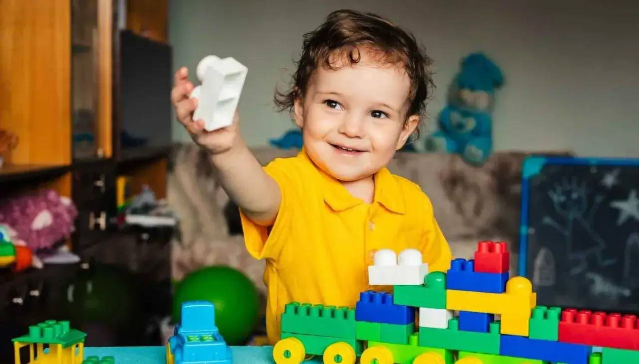 Un ni&ntilde;o de 2 a&ntilde;os sonr&iacute;e mientras juega con bloques de construcci&oacute;n, creando un tren colorido.