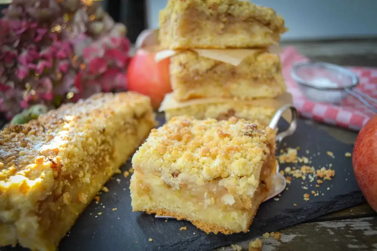 Saftiger Apfelmuskuchen vom Blech mit Streuseln, wie von Oma gebacken. Ein Stück davon liegt auf einer Kuchenschaufel.