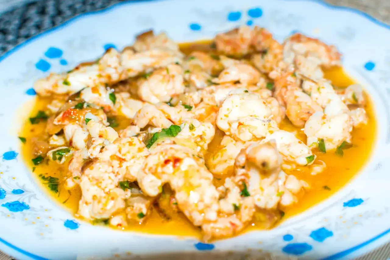 Plato de cigalas al ajillo, con trozos de ajo y perejil picado en una salsa dorada.