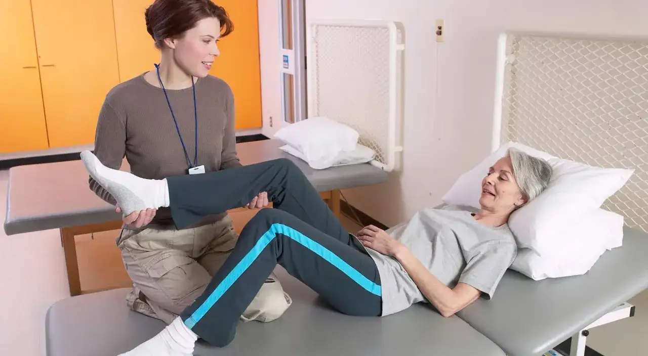Fizjoterapeutka pomaga starszej kobiecie w ćwiczeniach, która odczuwa złe samopoczucie po zabiegach rehabilitacyjnych.