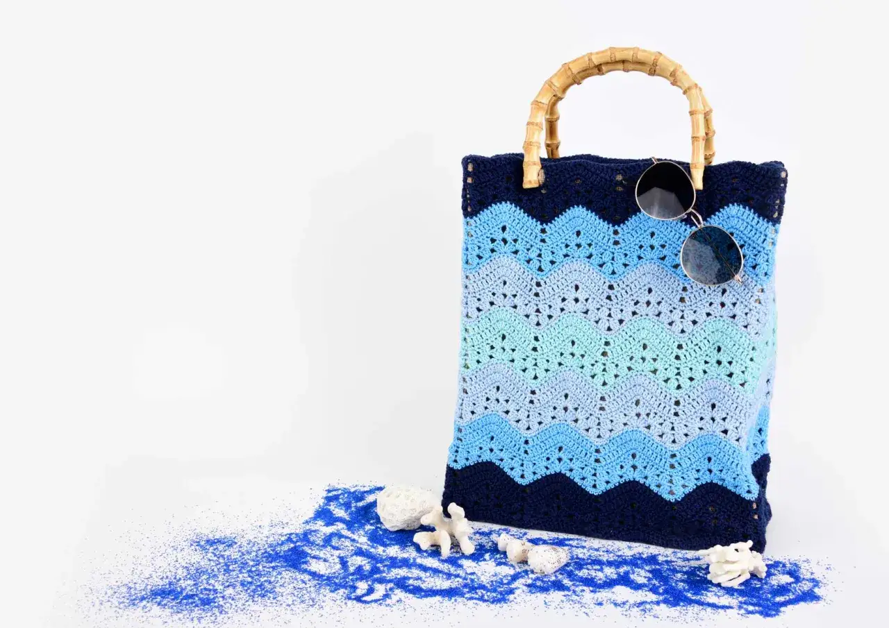 Borsa da spiaggia con manici in bambù, realizzata con lavori uncinetto cotone in sfumature di blu e azzurro. Decorata con conchiglie e sabbia blu.