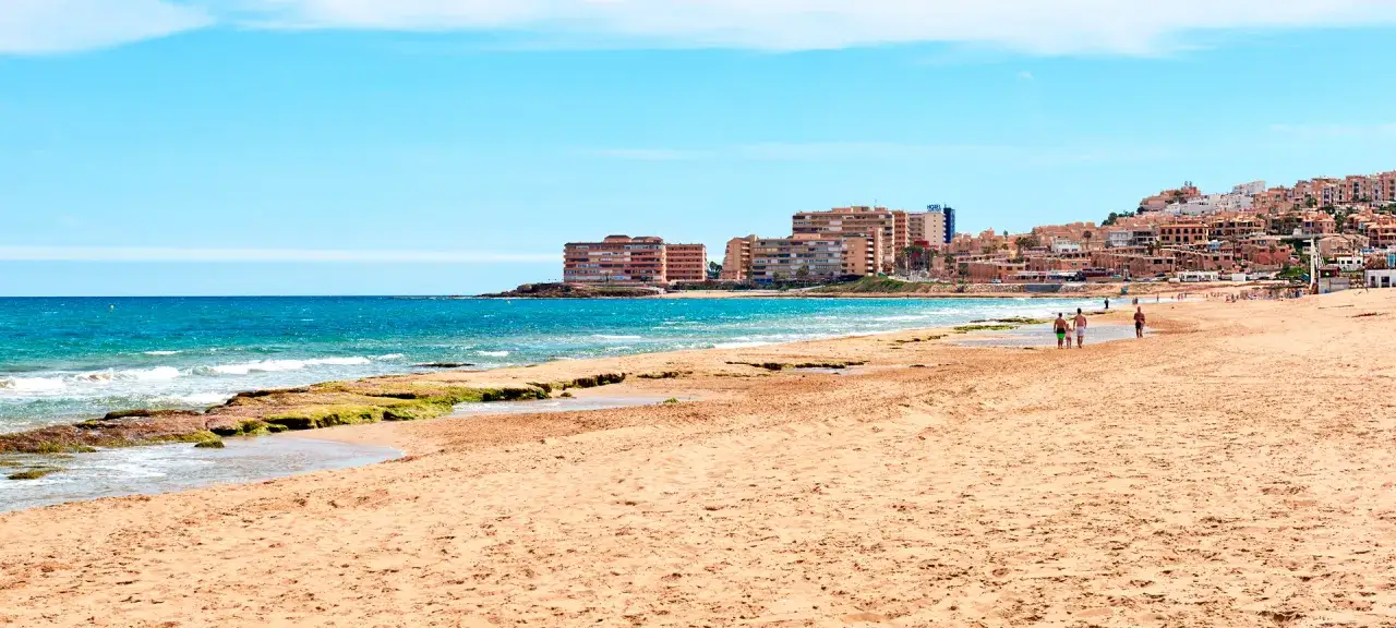 Sonniger Strand an der playa de la mata mit sanften Wellen und einer Stadtkulisse im Hintergrund.