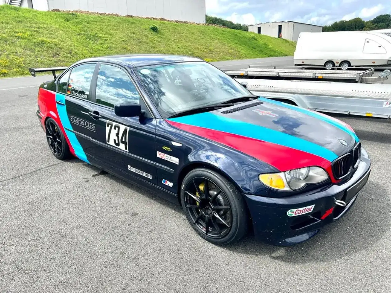 Mroczne BMW E46 330i z numerem 734 i kolorowymi pasami na masce, gotowe do wyścigu.