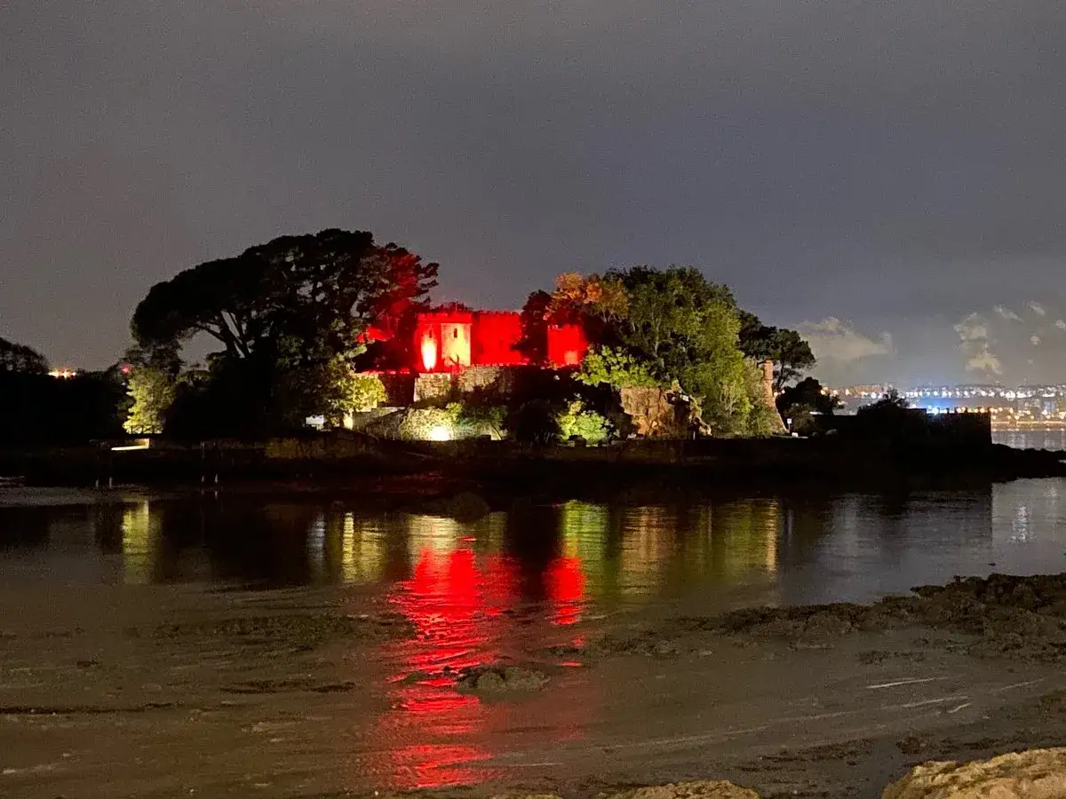 El castillo de Santa Cruz, iluminado en rojo, se refleja en el agua nocturna.