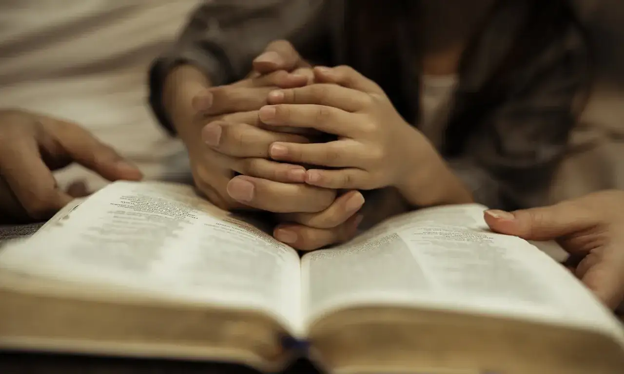Hands clasped over an open Bible, a family finds peace and freedom in Christ.