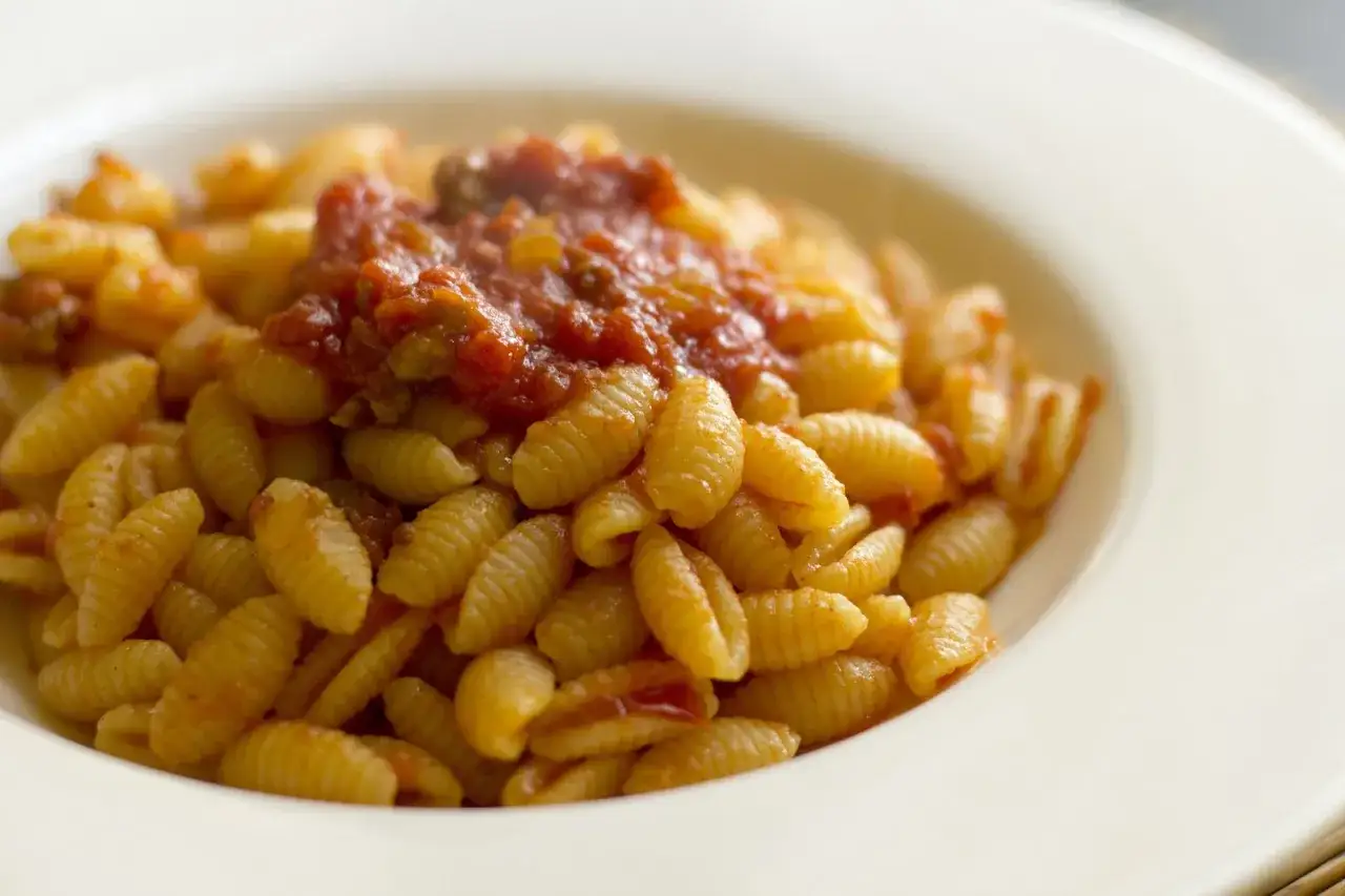 Un piatto invitante di malloreddus alla campidanese, pasta saporita con sugo rosso e carne.