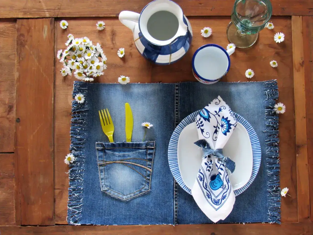 Tovagliette americane fai da te in denim con tasca porta posate, decorate con margherite e un servizio da tavola blu e bianco.