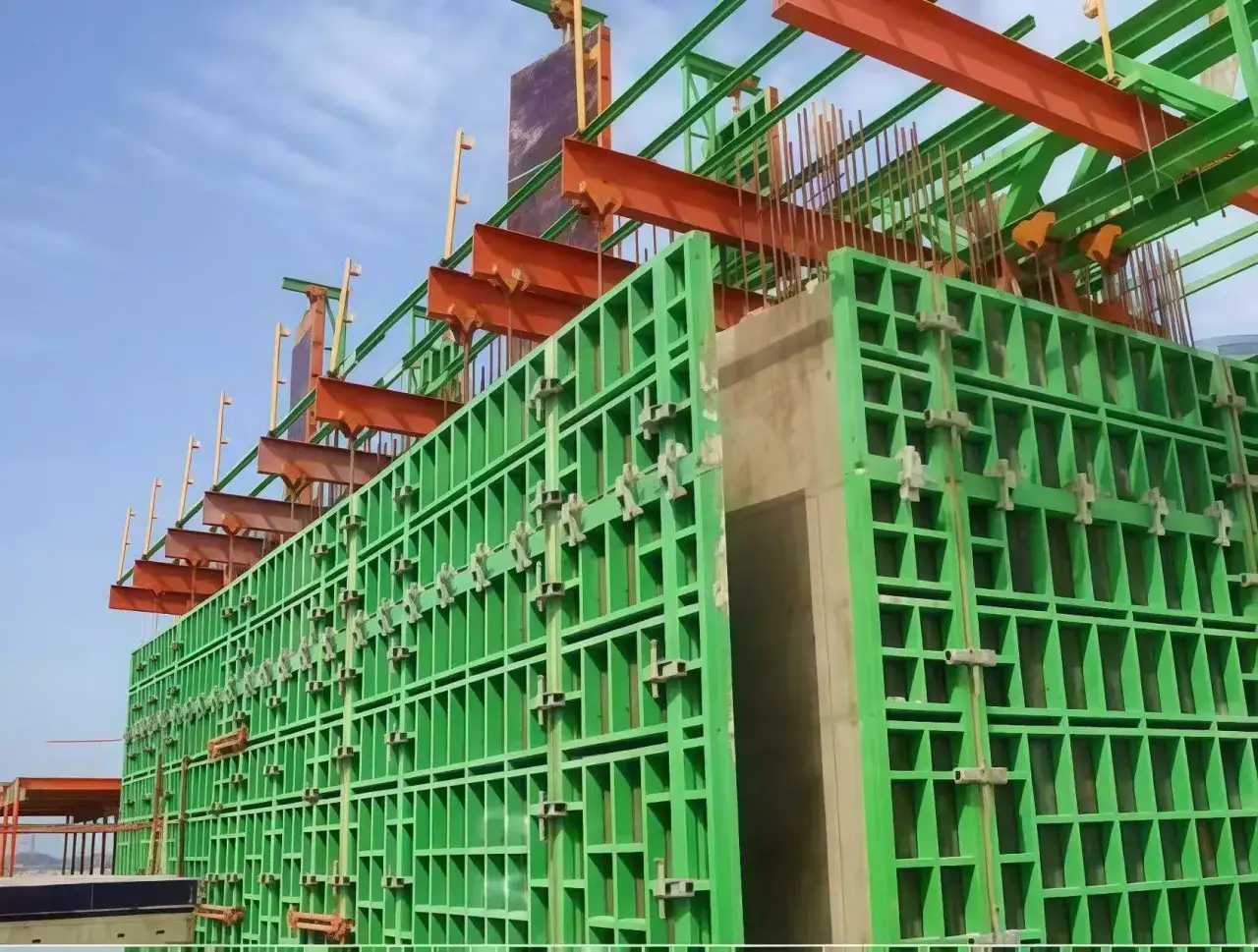 Estructura verde de encofrado en construcci&oacute;n, lista para verter hormig&oacute;n. Se aprecian vigas naranjas y barras de acero.