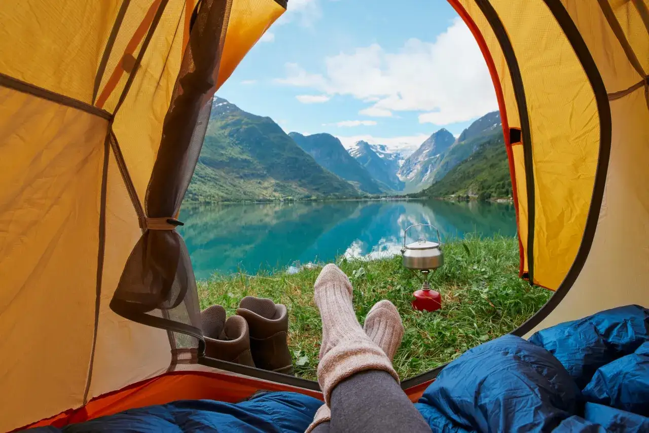 Vila i tält med utsikt över en turkos sjö och snöklädda berg. Perfekt för campingplatser i Norge.