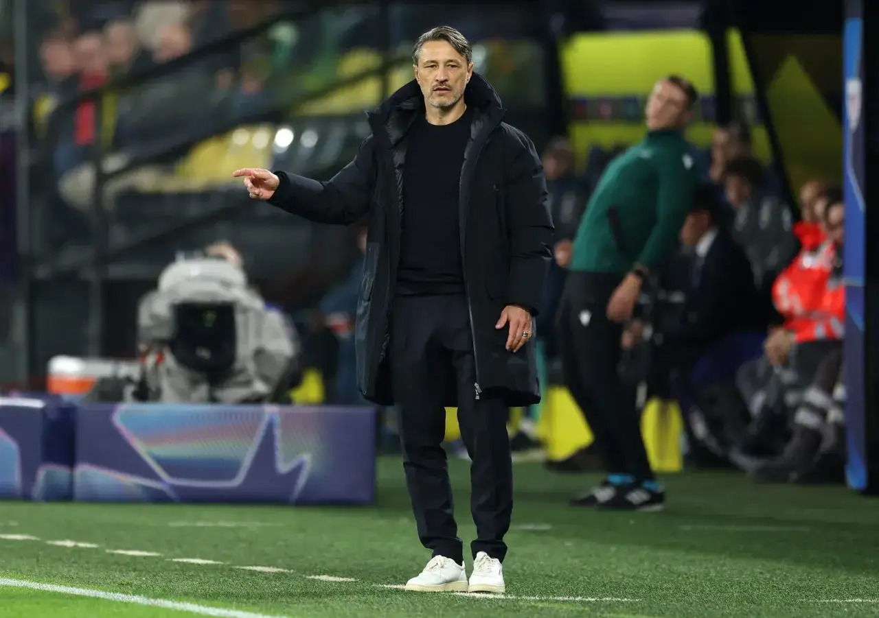 Trener Borussii Dortmund w czarnej kurtce i spodniach wskazuje palcem, analizując grę na boisku.