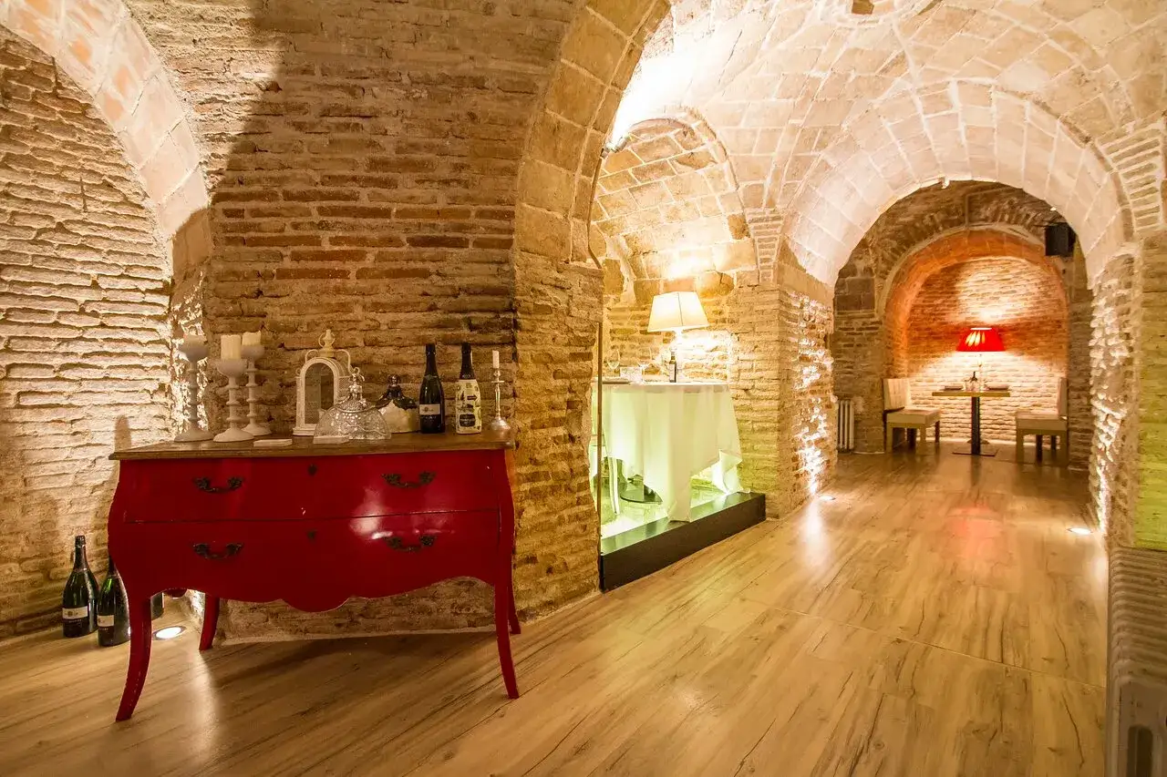 Bodega con arcos de ladrillo, cómoda roja, botellas de vino y mesas dispuestas para una cena íntima. Aquí se guardan las opiniones de bodega de los secretos.