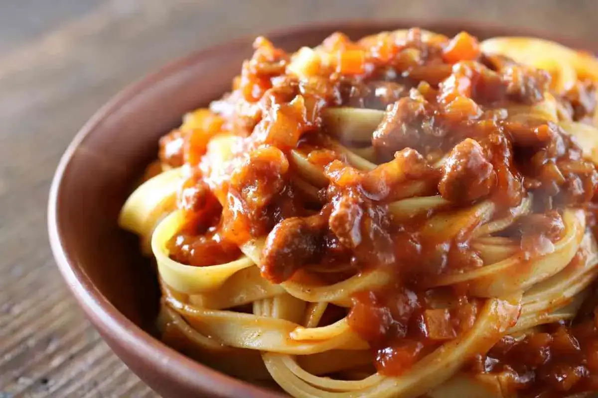 Tagliatelle al ragù, un classico dei primi piatti di carne, servite in una ciotola di terracotta su un tavolo di legno.