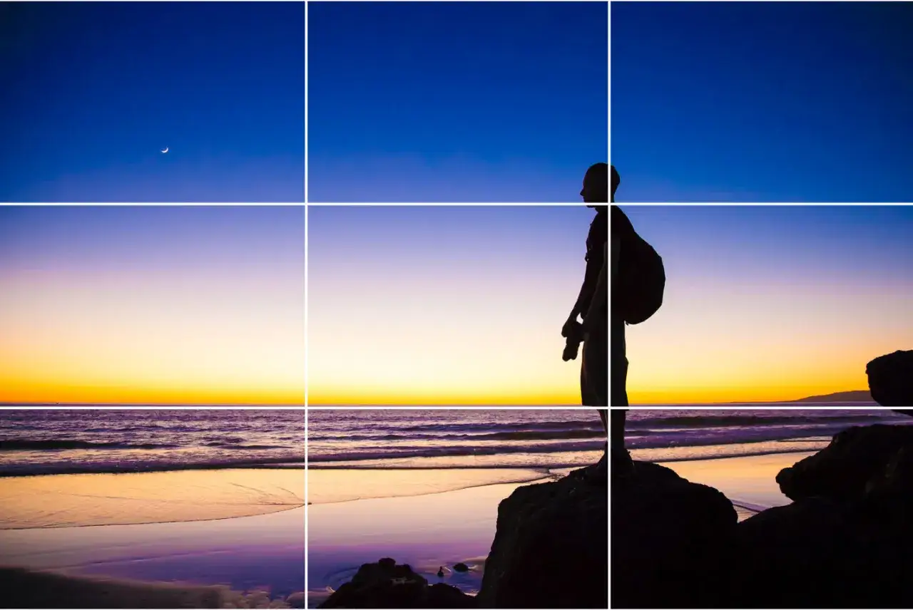 Silueta de fot&oacute;grafo en la playa al atardecer, con la luna creciente. Una escena inspiradora para fotograf&iacute;a para principiantes.