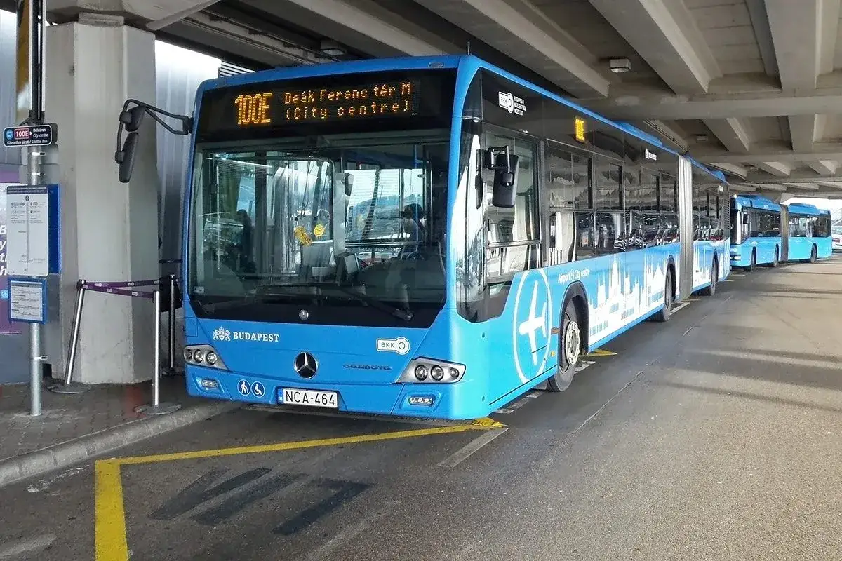 Blå buss 100E på Budapest flygplats till centrum. Flera bussar i kö under en betongkonstruktion.