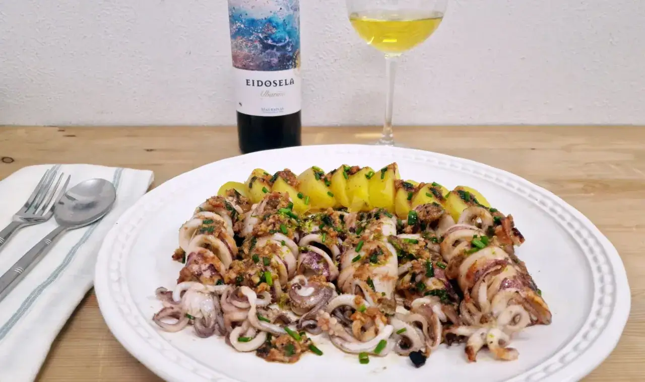 Calamares a la riojana con patatas, servidos en plato blanco, acompa&ntilde;ados de vino Albari&ntilde;o y cubiertos con perejil picado.