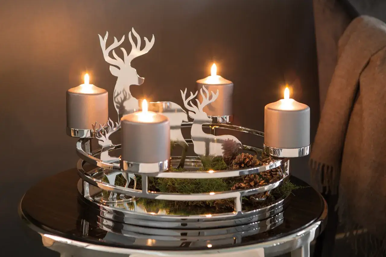 Moderner Adventskranz-Trend: Vier graue Kerzen auf einem silbernen Hirsch-Gestell mit Moos und Zapfen.