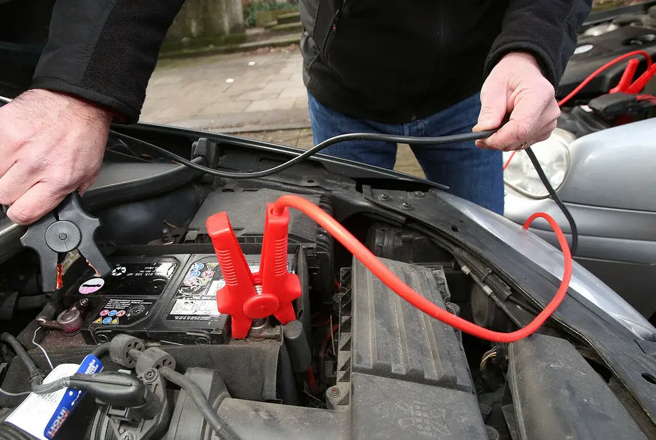 Starthilfe: Warum nicht minus an minus? Jemand klemmt Starthilfekabel an eine Autobatterie.