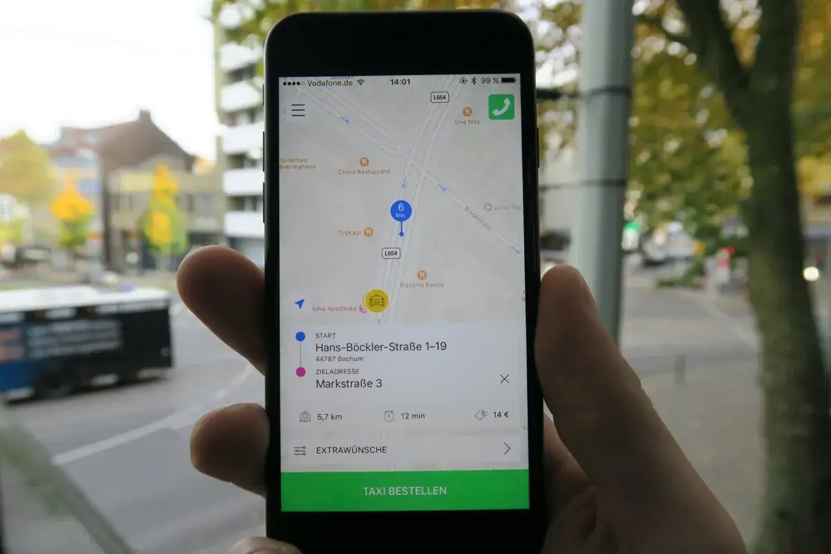 Hand h&auml;lt Smartphone mit Taxibestellung. Bezahlung per PayPal ist m&ouml;glich.
