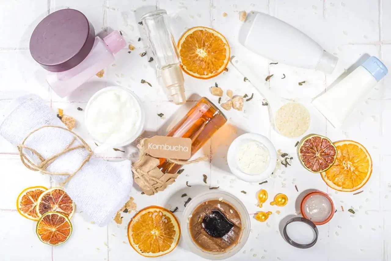 Kombucha-Flasche mit Etikett, daneben eine Sch&uuml;ssel mit wei&szlig;er Creme, getrocknete Orangen und ein Handtuch. Leuconostoc/Radieschenwurzel-Fermentfiltrat f&uuml;r die Hautpflege.