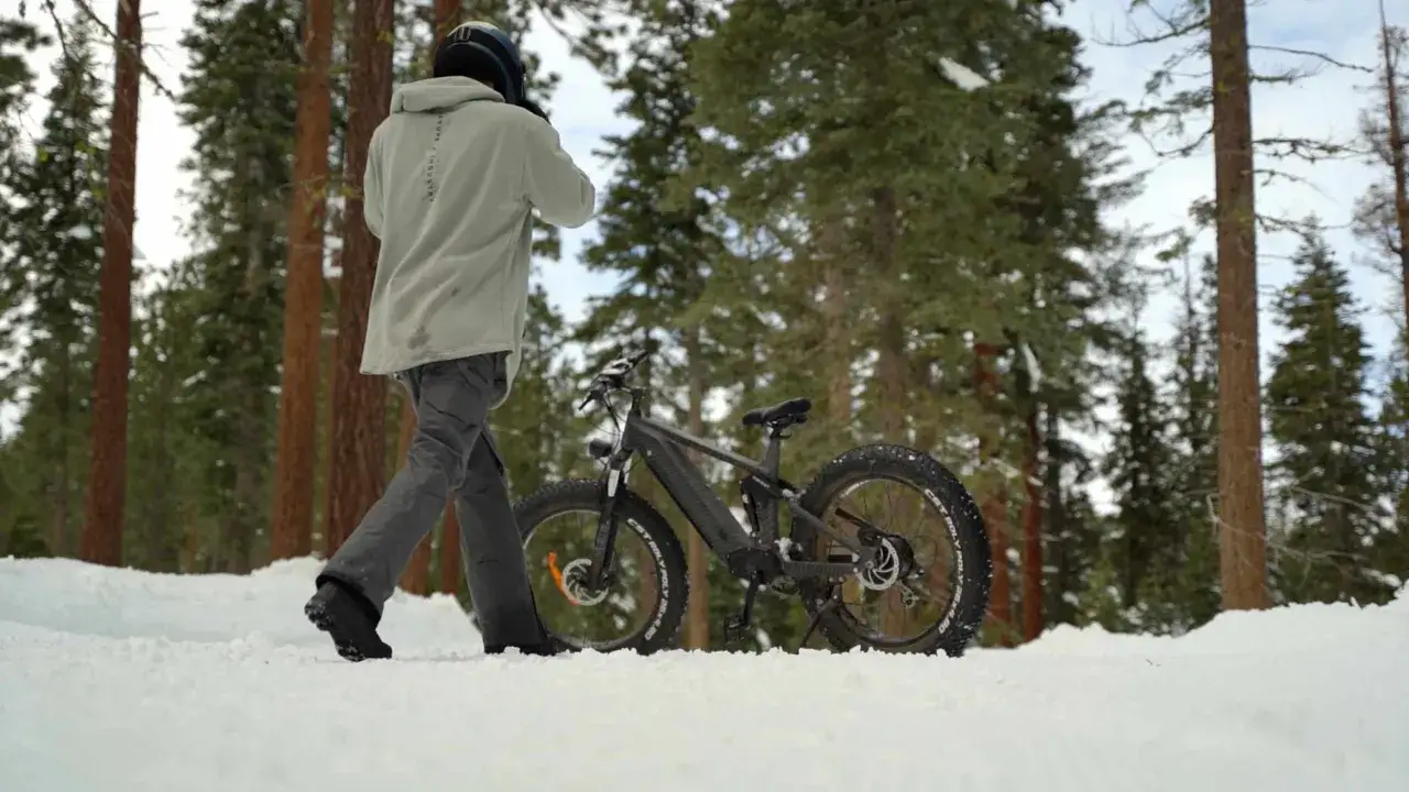 Man met helm loopt naast fatbike in de sneeuw. Goed om de **fietsaccu bewaren in de winter** op een droge plek.