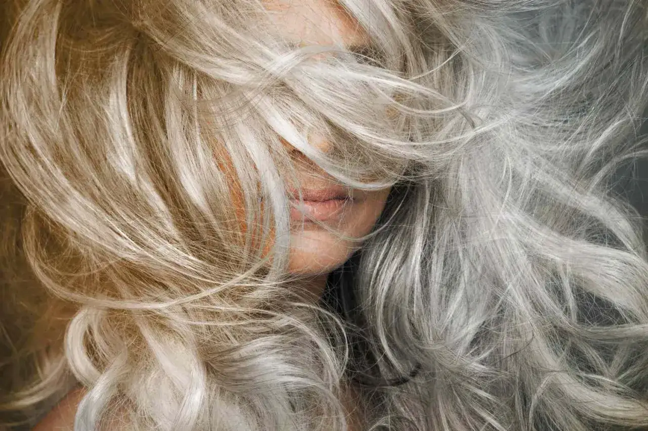 Kobieta z burzą włosów w odcieniach blond i siwych, tworzących efekt **grombre**.
