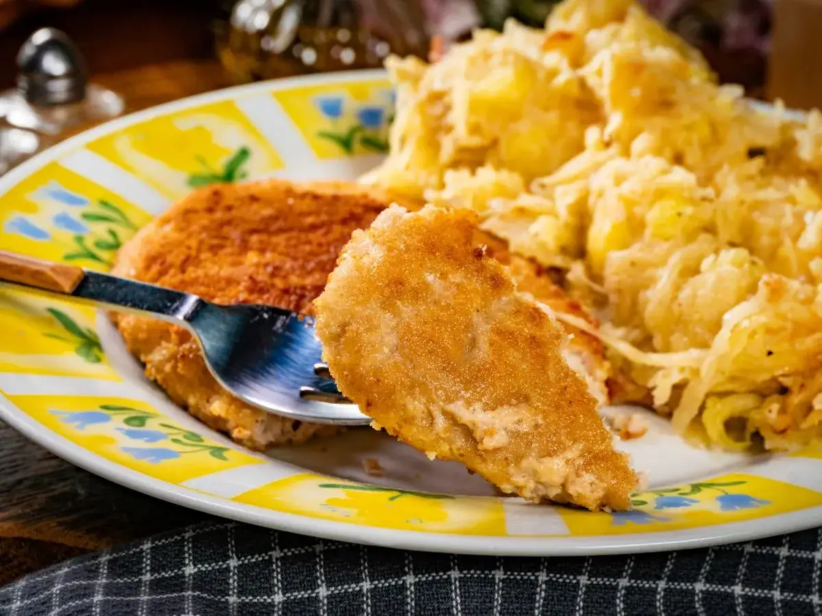 Złocisty kotlet po parysku, chrupiący z wierzchu, podany z porcją tartej kapusty. Widok z bliska na talerzu.