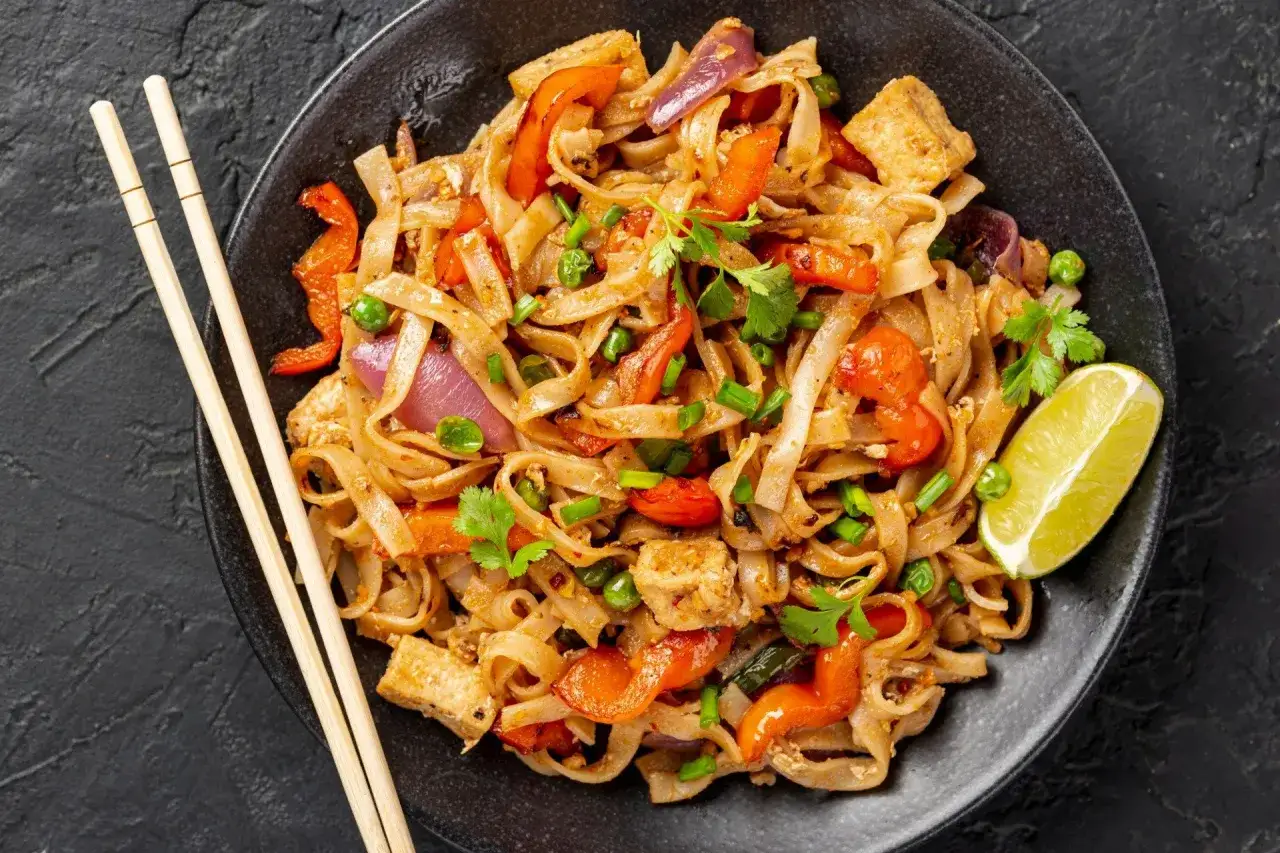 Pyszny pad thai z kurczakiem, warzywami i makaronem ryżowym, udekorowany kolendrą i ćwiartką limonki.