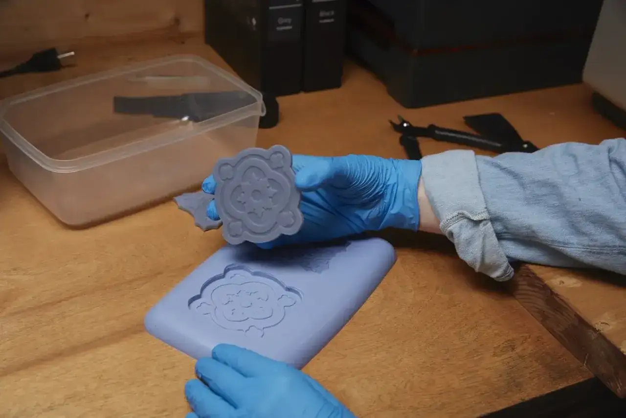 Manos con guantes azules manipulan un molde de silicona con dise&ntilde;o floral. Se muestra c&oacute;mo hacer moldes de silicona.
