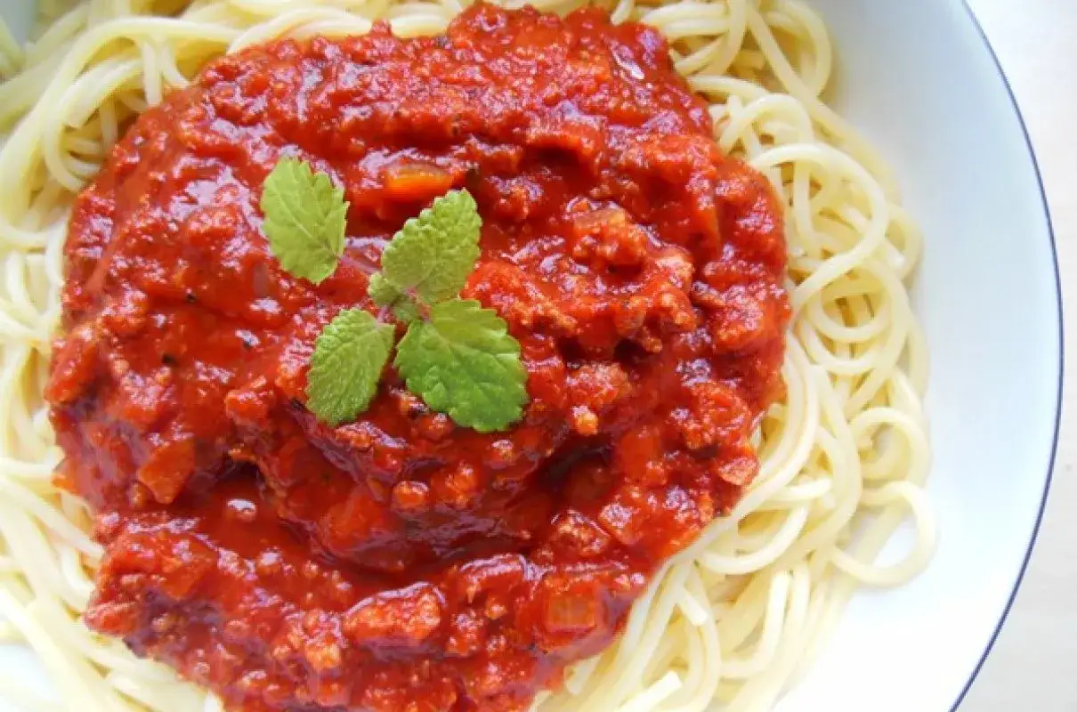Porcja spaghetti z mięsem mielonym w sosie pomidorowym, udekorowana listkami mięty.