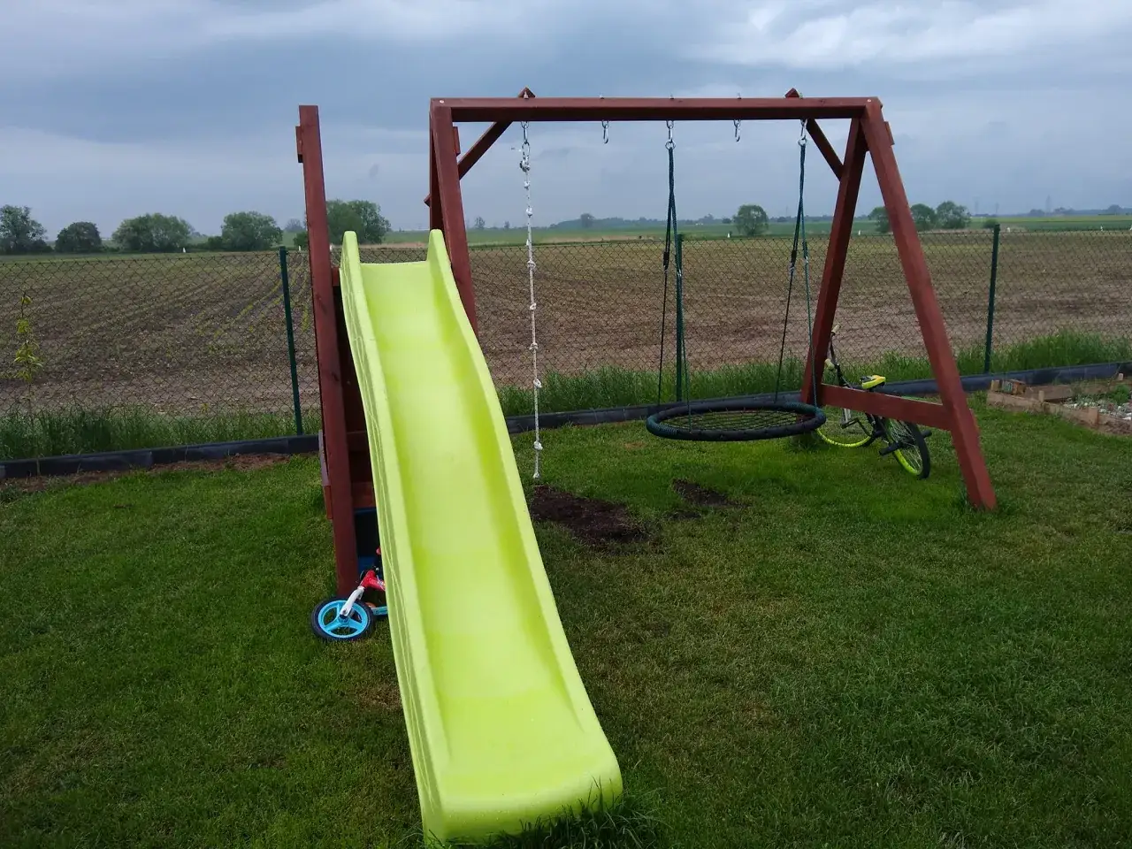 Jak urządzić mały plac zabaw dla dzieci: zjeżdżalnia, huśtawka i rower biegowy tworzą idealne miejsce do zabawy na świeżym powietrzu.