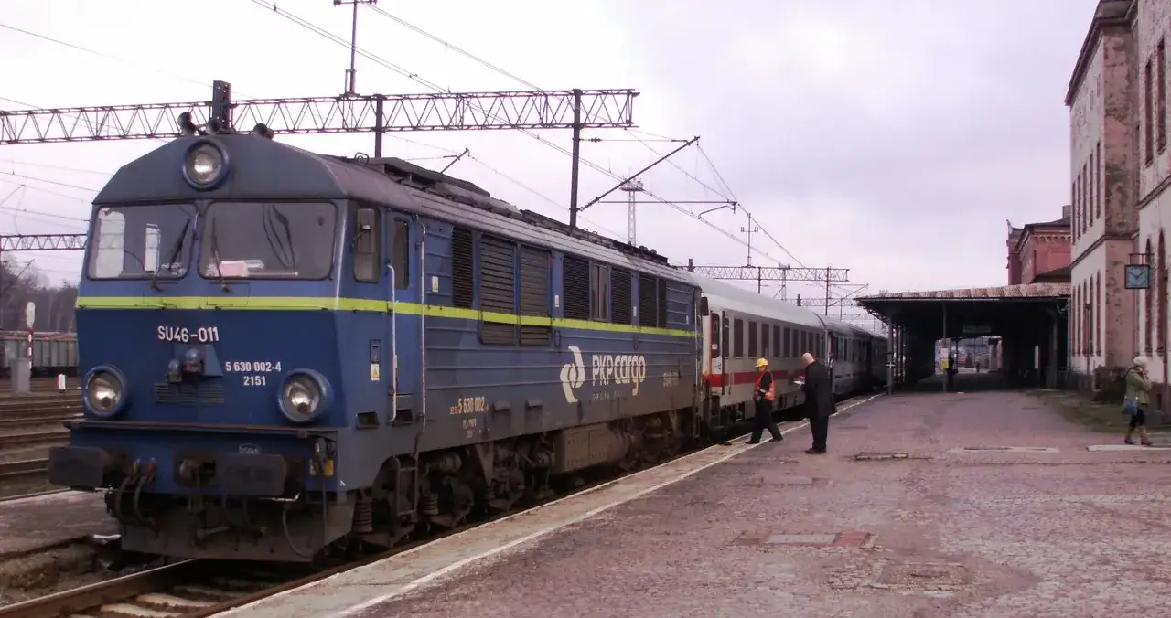 Eine blaue Lokomotive der PKP Cargo steht am Bahnsteig. Ein Zug f&auml;hrt nach Polen.