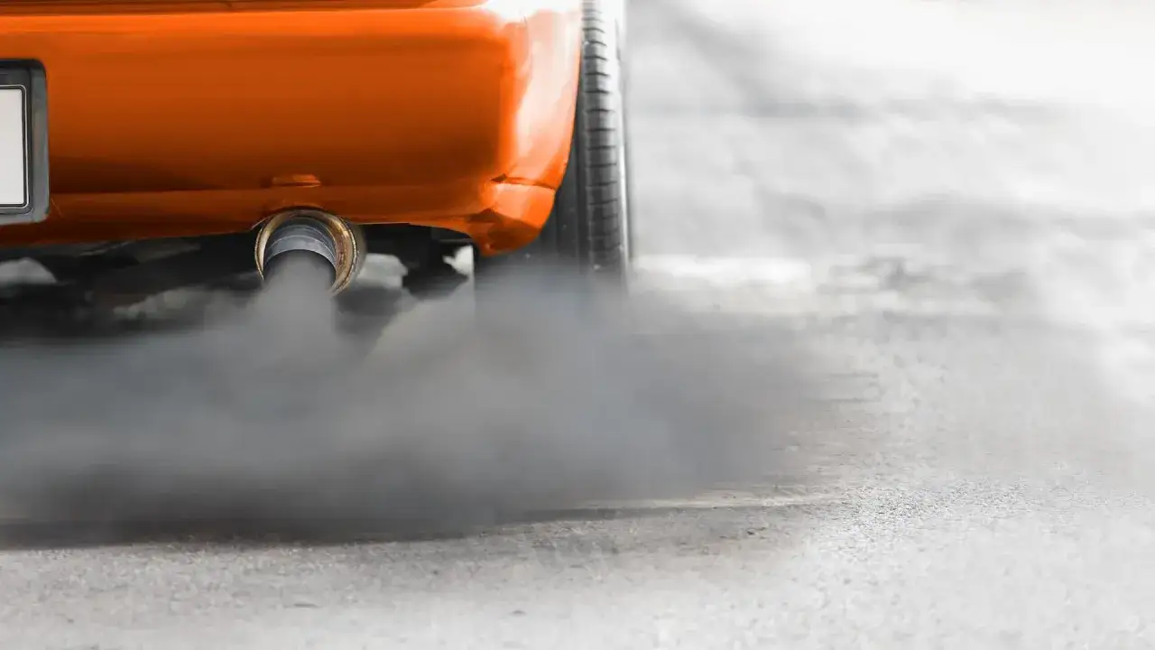 El tubo de escape de un coche naranja emite una densa nube de humo negro, contaminando el aire.