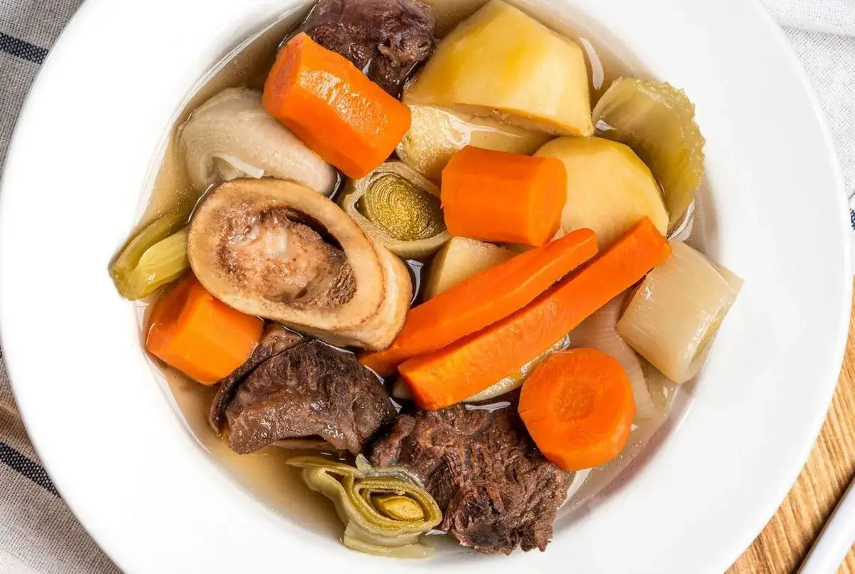 Un plat réconfortant de pot-au-feu, avec des morceaux de bœuf, des carottes, des pommes de terre et des poireaux, digne d'une recette du Journal des Femmes.