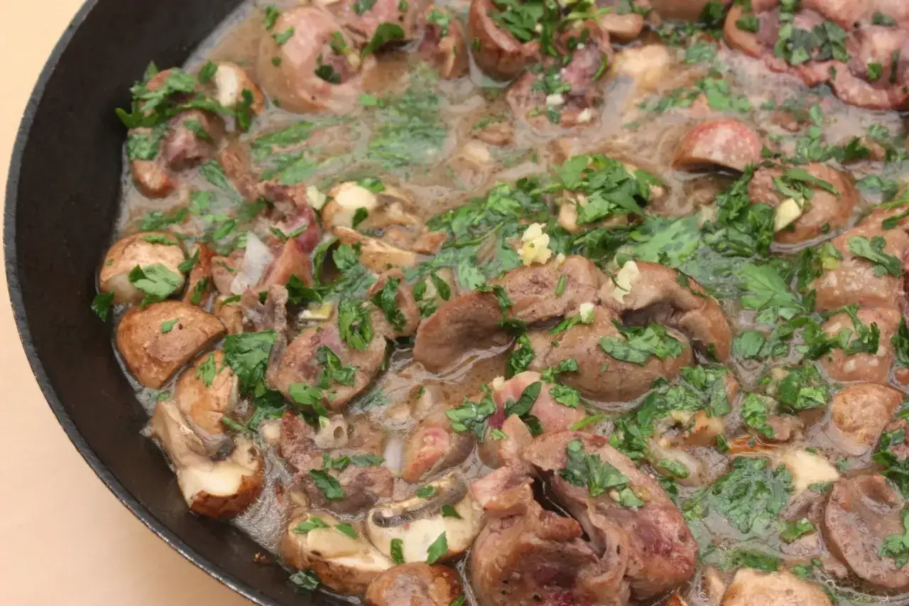 Rognon de veau mijoté avec des champignons et du persil frais dans une poêle.