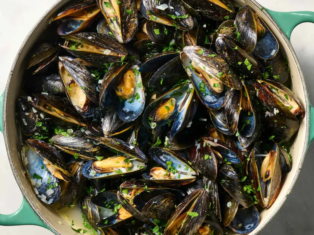 Mejillones al vapor reci&eacute;n cocinados, conchas abiertas mostrando su jugosa carne, espolvoreados con perejil fresco y trocitos de ajo.