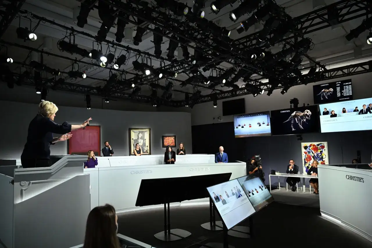 An auctioneer leads a sale at Christie's, with screens displaying auction items and prices. This scene captures the excitement of Christie's news.