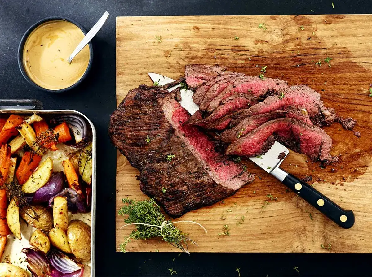 Saftig flankstek ugn, skivad och serverad med ugnsrostade rotfrukter och en krämig sås.