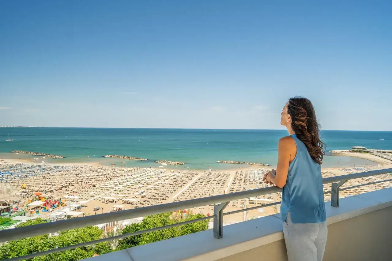 Vista dalla terrazza dell'hotel Acropolis Cattolica: una donna ammira la spiaggia affollata e il mare azzurro.