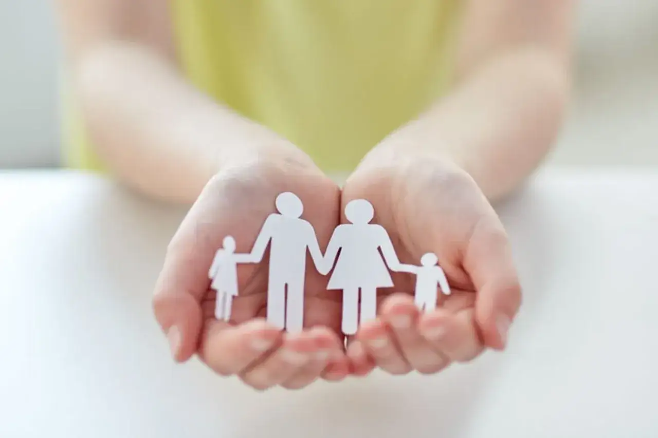 Mains tenant une famille en papier, symbole d'une lettre de demande d'agrément adoption.