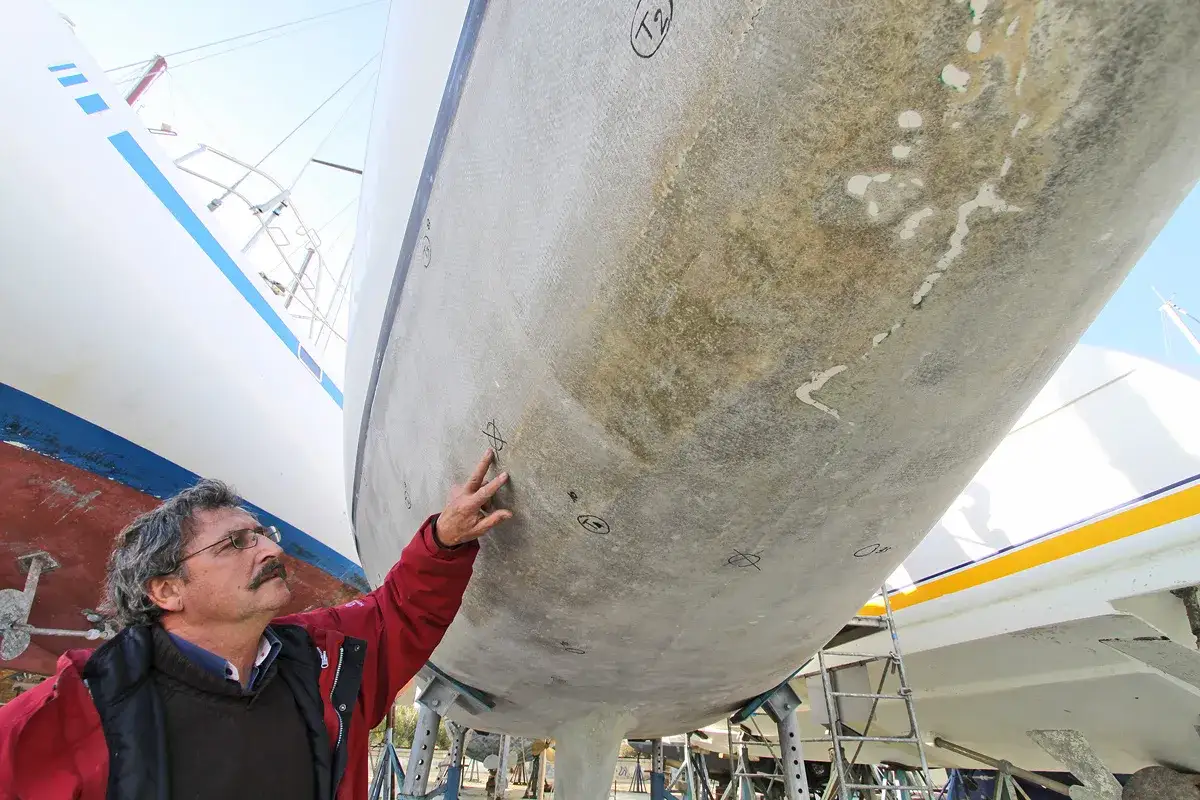 Un homme inspecte la coque d'un bateau, marquant des points pour des retouches marines.