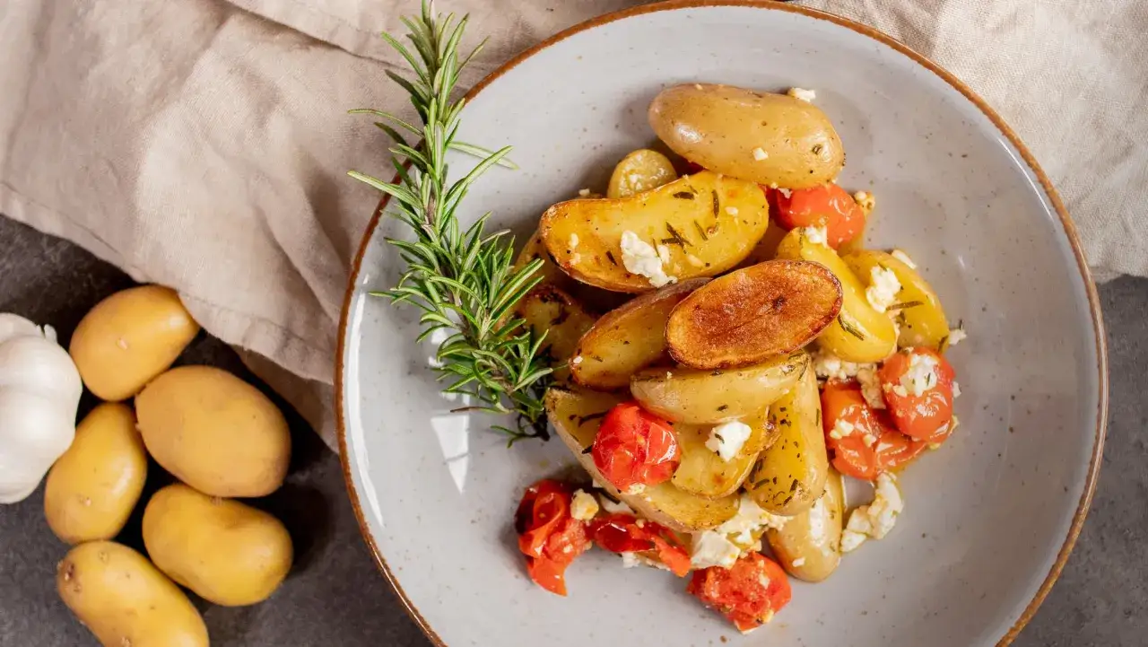 Köstliche Drillinge kochen mit Rosmarin, Kirschtomaten und Feta. Daneben liegen rohe Kartoffeln und Knoblauch.