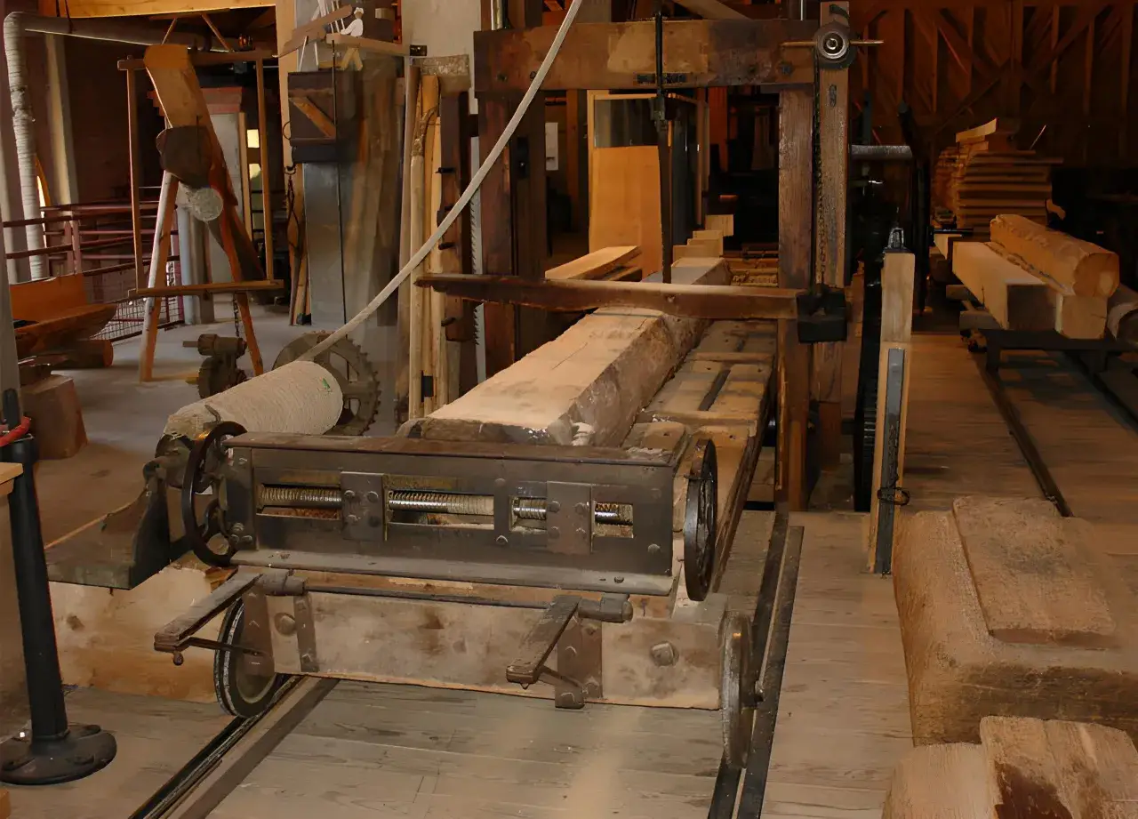 Scierie ancienne avec une grosse pièce de bois sur un chariot. L'ensemble évoque le savoir-faire d'une marque outillage français.