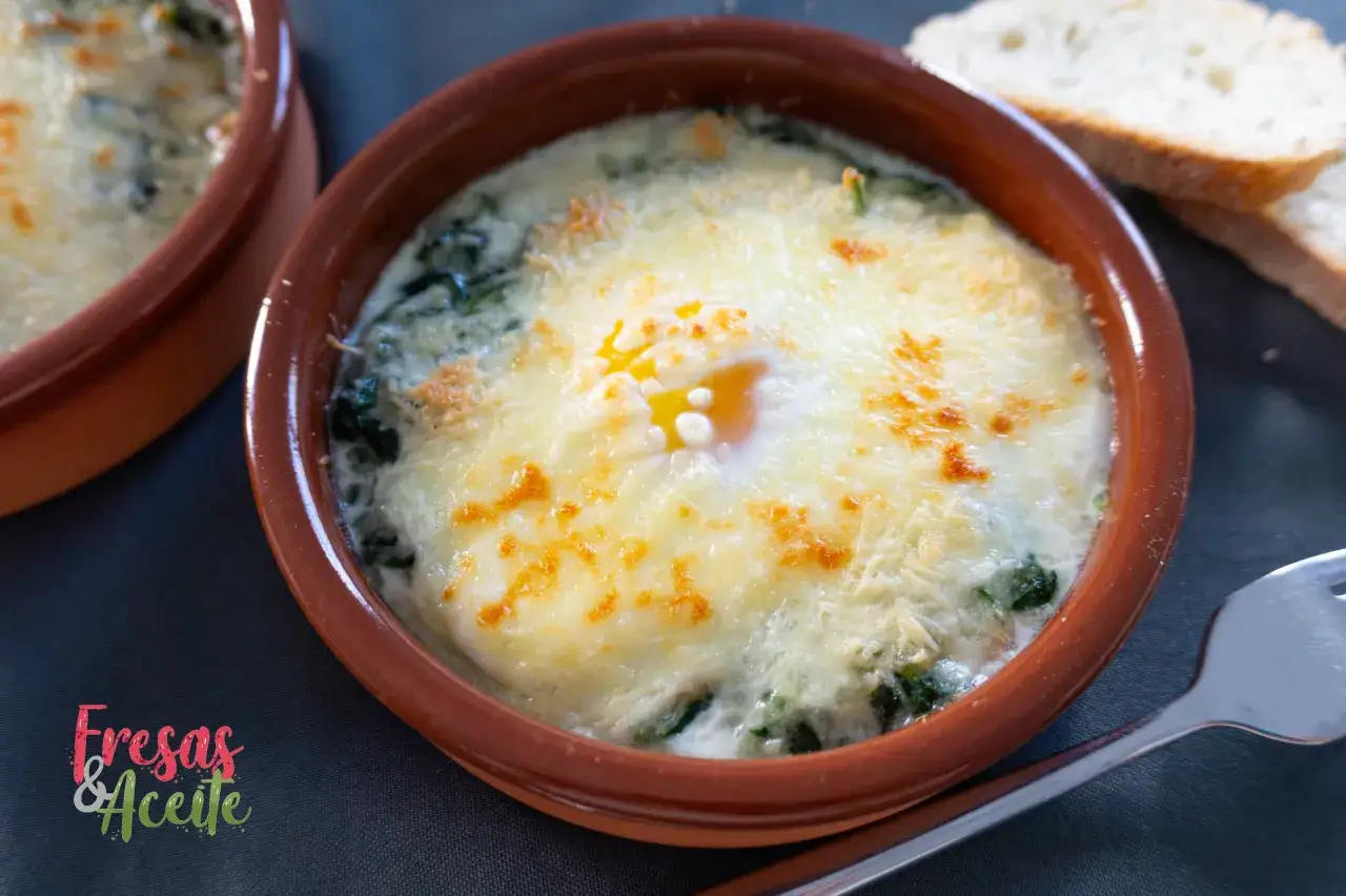 Un huevo horneado sobre espinacas a la crema, gratinado con queso y acompañado de pan tostado.