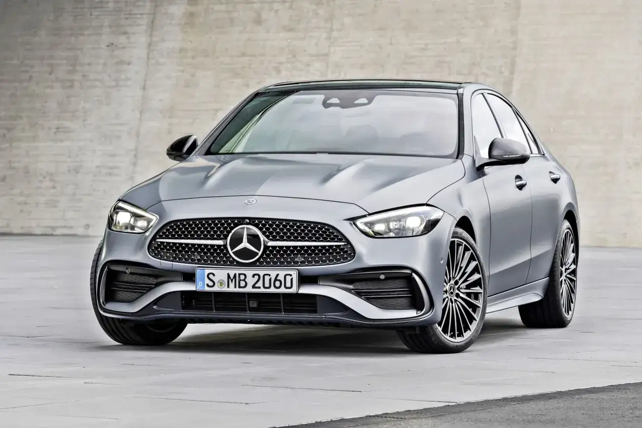 Elegancki, srebrny Mercedes-Benz Klasy C z charakterystyczną atrapą chłodnicy i nowoczesnymi światłami, zaparkowany na tle betonowej ściany.
