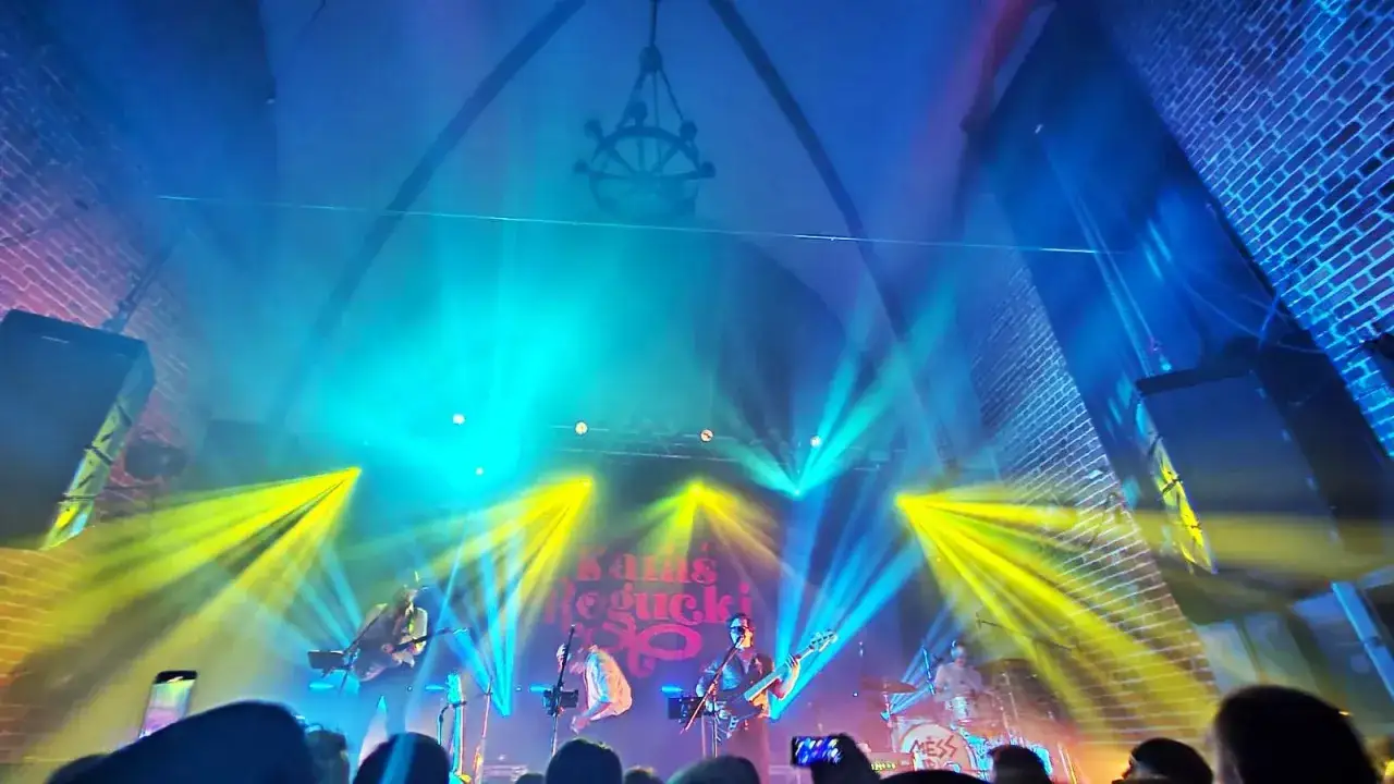 Koncert Karaś/Rogucki w Mariannie. Scena oświetlona ż&oacute;łtymi i niebieskimi światłami, zesp&oacute;ł gra dla publiczności.