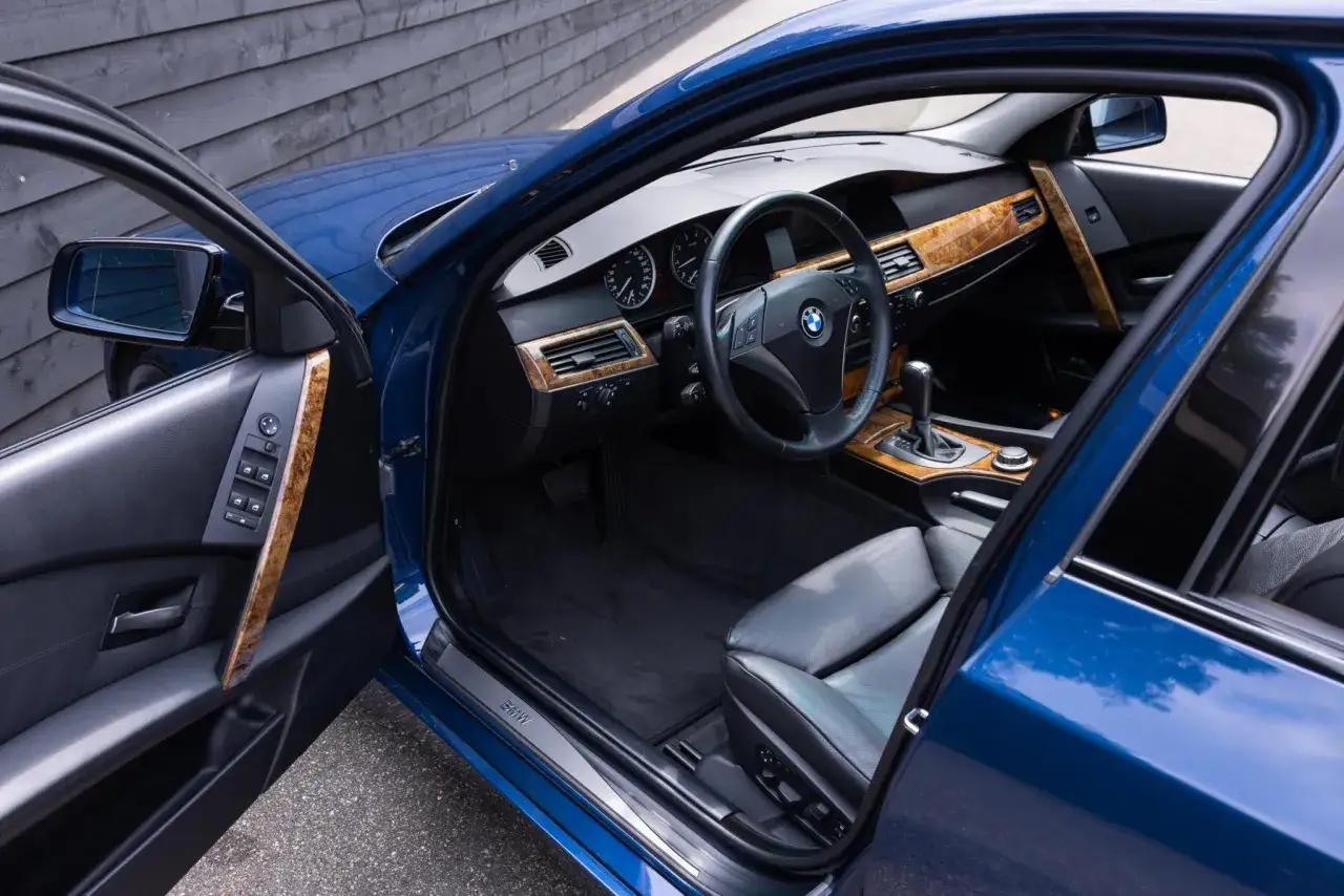 Wnętrze niebieskiego BMW 5 Series (E60) z drewnianymi wstawkami i czarną skórzaną tapicerką.