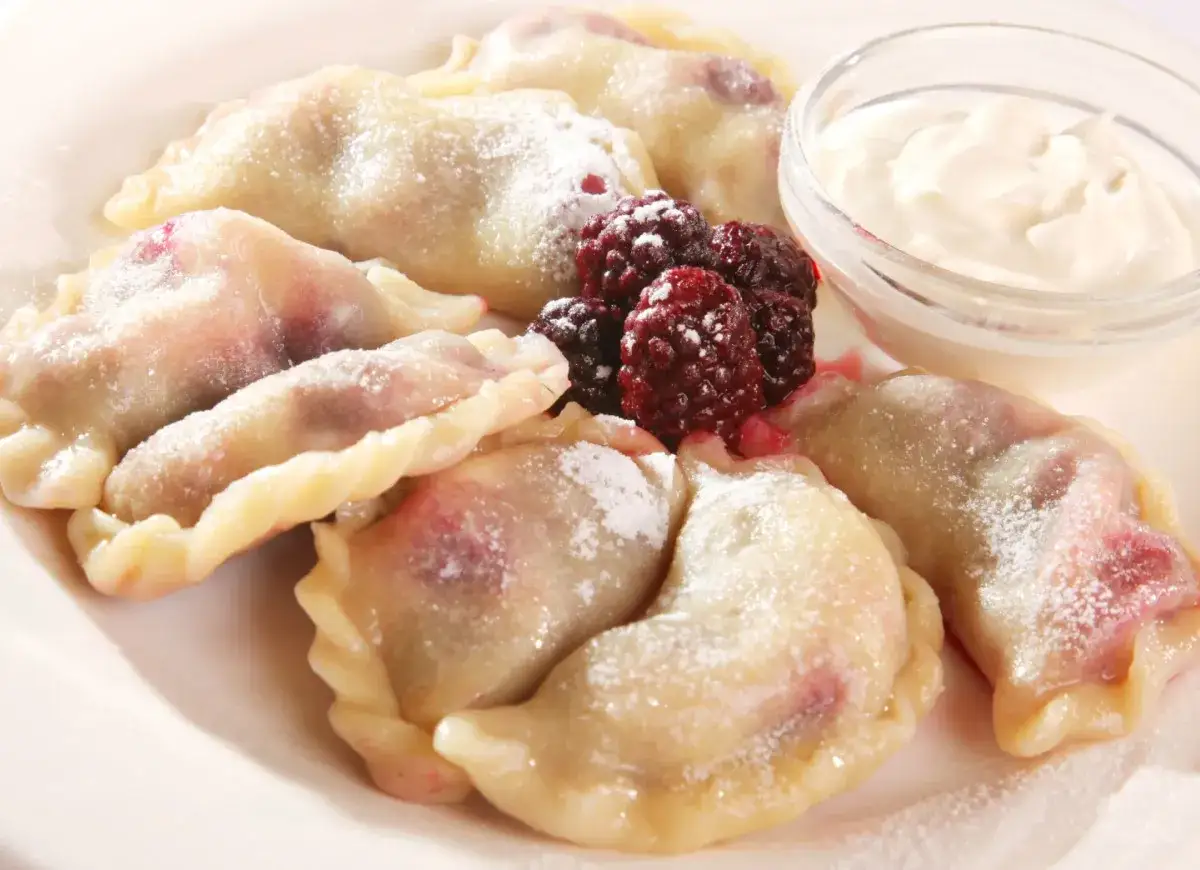 Pyszne pierogi z malinami, posypane cukrem pudrem, podane z kwaśną śmietaną i świeżymi malinami.