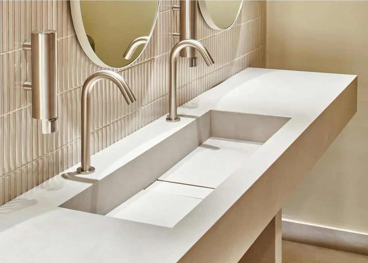 Lavabo integrato in **Dekton o gres**, con rubinetti a cascata e specchi rotondi.