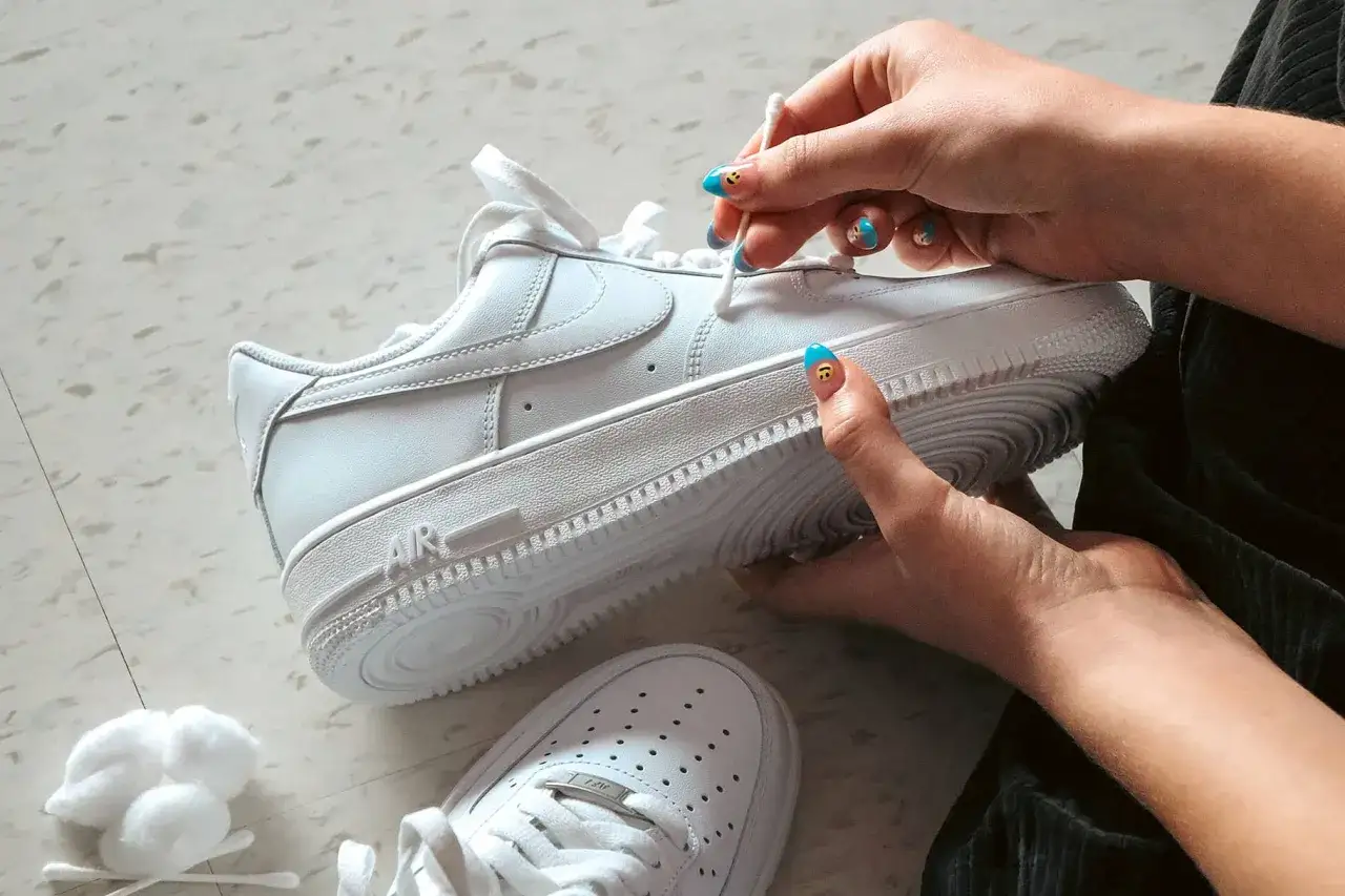 Main blanche, une personne nettoie une chaussure qui couine avec un coton-tige.