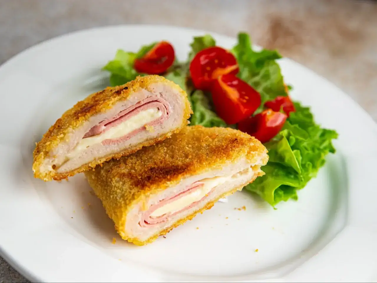 Pyszne cordon bleu przepis: panierowany kotlet z szynką i serem, podany z sałatką i pomidorkami.
